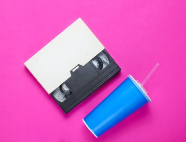 Saman ile kağıt bardak, pembe arka plan üzerinde video kaset. Pop kültürü 80'ler, retro tarzı. Üst te. Minimalizm