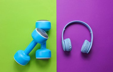 Yaratıcı konsept fitness. Plastik mavi halterler, yeşil, mor arka planda kulaklıklar. Minimalizm, üst görünüm, düz yatıyordu