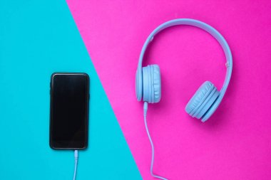 Akıllı telefona pembe-mavi arka planda bağlanan kulaklıklar. Minimalizm, üst görünüm
