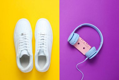 Retro tarzı. 80'li yıl. Minimalizm. Ses kasetli kulaklıklar, mor-sarı arka plana karşı beyaz spor ayakkabılar. Üstte görüntü