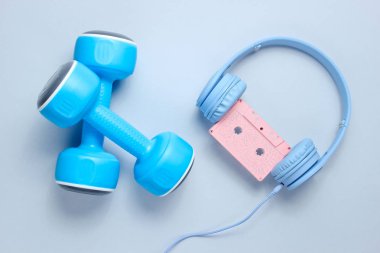 Spor ekipmanları. Retro tarzı. Mavi plastik halterler, gri arka planda ses kasetli kulaklıklar. Üstte görüntü.