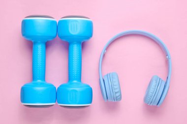 Mavi kulaklıklar, pembe pastel arka plan üzerinde plastik halter. Müzikle spor. Üstte görüntü.