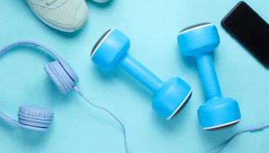 Spor konsepti. Kulaklık, plastik halter, mavi arka plan üzerinde spor spor ayakkabıları ile akıllı telefon Düz yatıyordu. Üstte görüntü