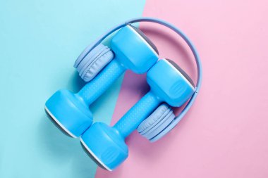 Minimalizm. Mavi kulaklıklar, mavi pembe arka plan üzerine plastik halterler. Müzikle spor. Düz yatıyordu. Üstte görüntü.
