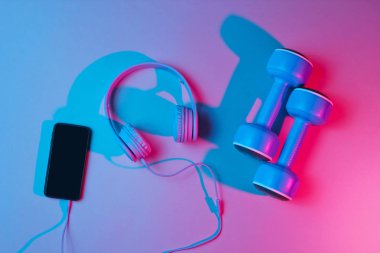 Yaşam tarzı konsepti. Kulaklıklı ve akıllı telefonlu dambıllar. Retro dalga, mavi kırmızı neon ışık, morötesi. Üst görünüm, minimalizm