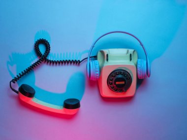 Kulaklıklı, eski model bir telefon. Retro dalga, kırmızı mavi ışık, ultraviyole. Üst görünüm, minimalizm