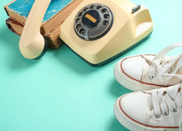Old sneakers, retro rotary phone and a stack of old phone books on mint color background