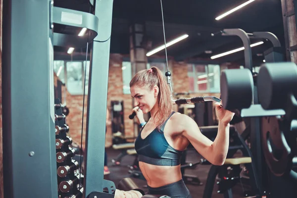 身材苗条的女人在健身房里用重型机械 运动观念 健身锻炼来训练她的后背 — 图库照片