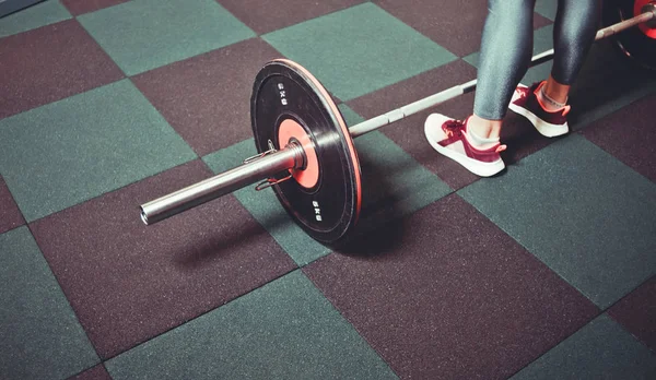 Woman trains in the gym with a barbell. Powerlifting. Heavy barbell on the floor and female leg