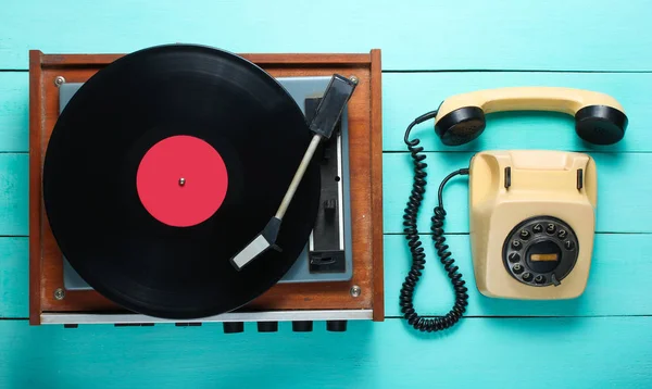 Vinyl player, rotary phone. Old-fashioned objects on a blue wooden background. Retro style, 70s. Top view.