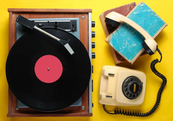 Old-fashioned objects on yellow background. Retro style, 80s, pop culture. Top view. Vinyl player, rotary phone, old books