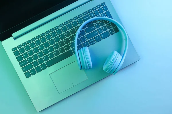 Modern laptop, wireless headphones. Gadgets. Neon night light, ultraviolet. Top view, minimalism