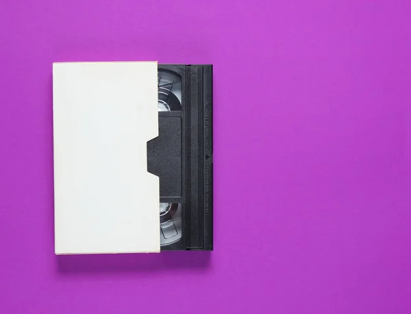 Mor arka plan daki kağıt kasadaki video kaset. Pop kültürü nitelikleri, minimalizm. Üstte görüntü