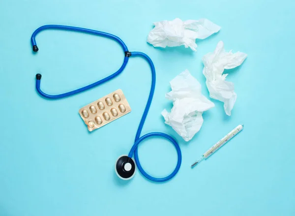 The concept of treating cold diseases. Used nasal wipes, thermometer, pills, stethoscope on blue background. Top view