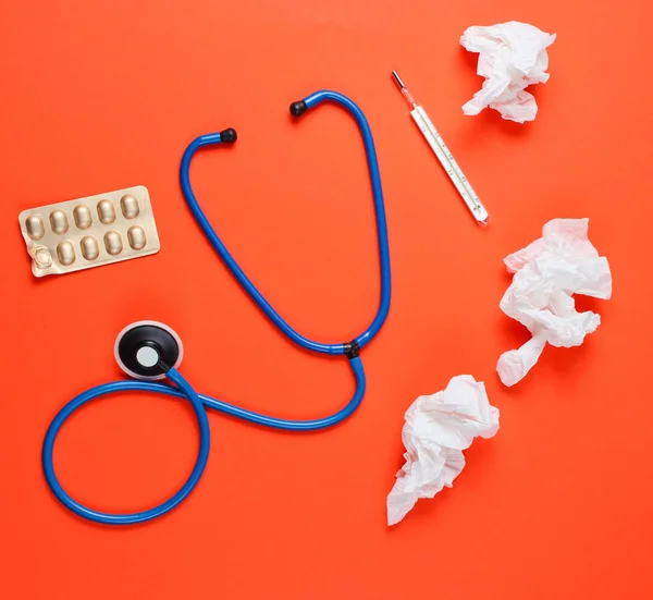 The concept of treating cold diseases. Used nasal wipes, thermometer, pills, stethoscope on orange background. Top view