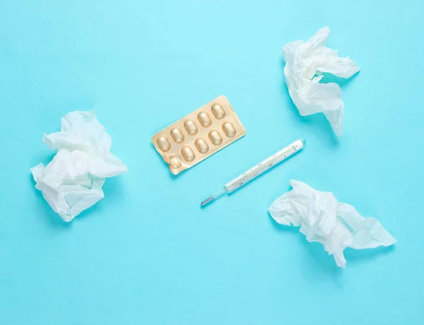 The concept of treating cold diseases. Used nasal wipes, thermometer, pills on blue background. Top view