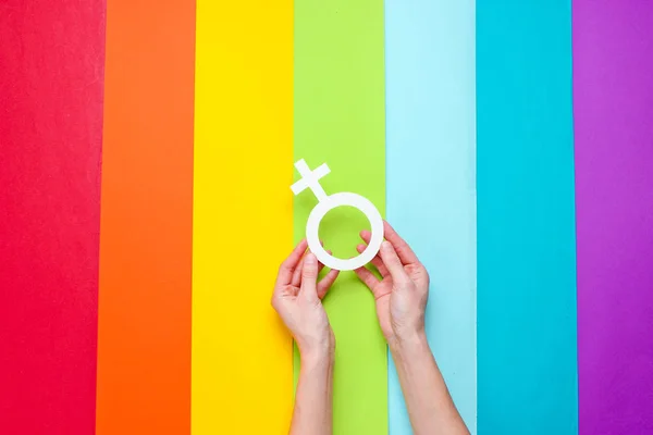 LGBT concept. Feminism. Minority sex. Gender equality. Hands holds female gender symbol on rainbow background. Top view, minimalism