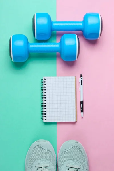 Fitness concept, workout plan. Plastic blue dumbbells, sport shoes, notepad on pastel background. Top view. Flat lay