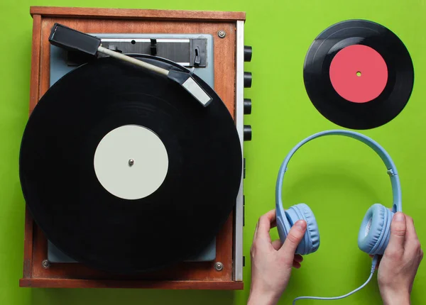 緑の背景にビニールレコードとレトロビニールレコードプレーヤーの背景にヘッドフォンを保持する女性の手 レトロなスタイル 80年代 トップ表示 — ストック写真