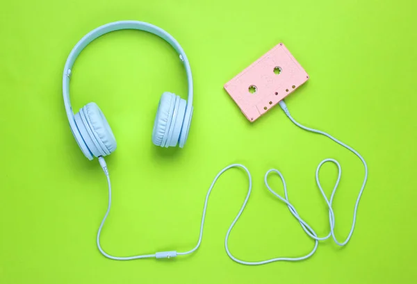 Blue headphones with cable in audio cassette on green  background. Minimalism. Top view