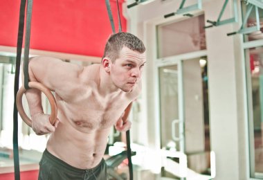 Çıplak gövde ile Kas adam spor salonunda jimnastik halkaları üzerinde egzersiz yapıyor