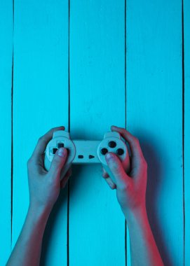 Konsept oyuncu. Gece hayatı. Eğlence. El mavi ahşap arka plan üzerinde gamepad tutar. Neon kırmızı mavi ışık. Retro tarzı. Üstte görüntü
