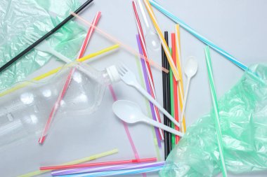 Kirlilik plastiği ve polietilen çevre kavramı. Selofan çanta, plastik şişe, tek kullanımlık çatal ve kaşıklar, gri arka planda kokteyl tüpleri. Üst görünüm