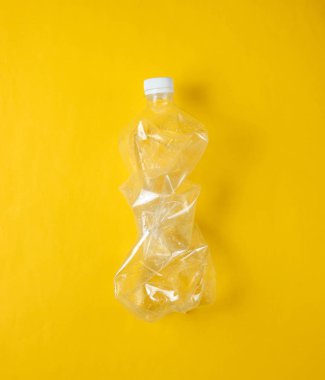 Minimalist ekolojik kavram. Sarı arka planda buruşuk plastik şişe. Çevre plastik kirliliği