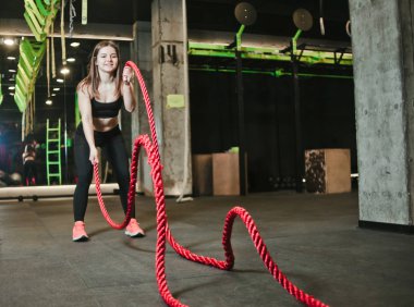 Antrenman konsepti. Jimnastik salonundaki halatlarla çalışan güçlü ve çekici bir genç kadın. Savaş halatıyla antrenman 
