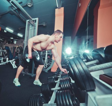 Genç, yakışıklı, yetişkin bir erkek modern spor salonunda tek kollu halterler çekiyor.