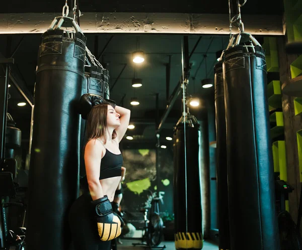 A tired young sport woman in boxing gloves  resting after  heavy boxing training with punching bag.
