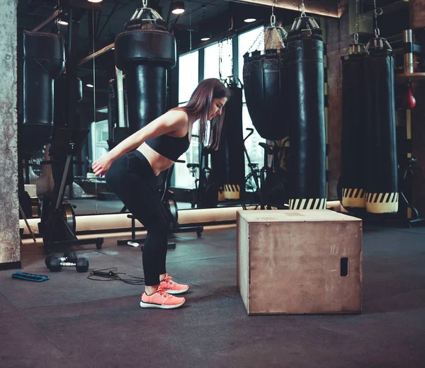 Fitness woman jumping on wooden box training at the gym, workout. Brunette girl in sportwear doing some jumping exercises in gym