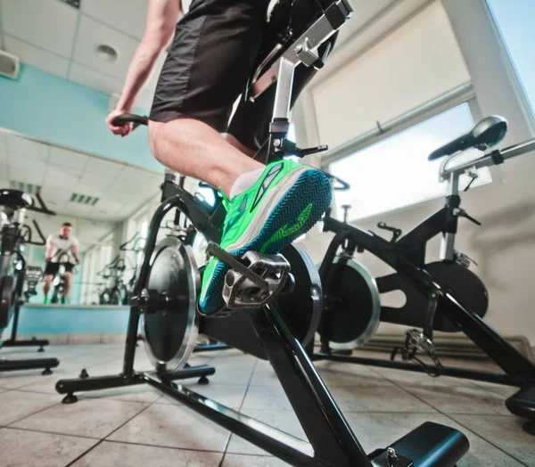 Spor ayakkabılı ve şortlu bir adamın geniş açılı görüntüsü bisiklet dersinde kardiyo bisikleti üzerinde egzersiz yapıyor. Sağlıklı yaşam tarzı kavramı