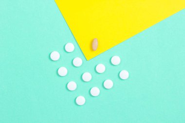 Asgari tıbbi konsept. Bir grup özdeş beyaz tablet ve pastel renkli arka plan üzerinde eşsiz bir tablet. Üst görünüm