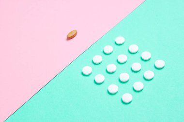 Asgari tıbbi konsept. Bir grup özdeş beyaz tablet ve pastel renkli arka plan üzerinde eşsiz bir tablet. Üst görünüm