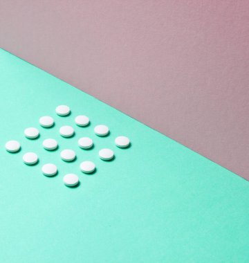 Asgari tıbbi konsept. Pastel renkli arka planda aynı beyaz tabletlerden oluşan bir grup. Üst görünüm