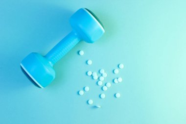 Minimalizm spor farmakolojisi konsepti. Mavi plastik dambıl ve beyaz anabolik haplar, mavi yeşil holografik ışık. Üst görünüm