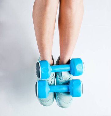Spor ayakkabılı kadın bacakları beyaz arka planda mavi plastik halterler tutuyor. Üst Manzara. Fitness minimalizmi