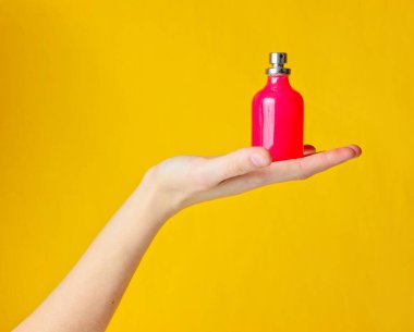 Avucunun içinde sarı arka planda bir parfüm şişesi tutan kadın.