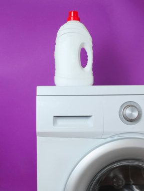 Çamaşır makinesinde mor arka planda bir şişe çamaşır jeli.