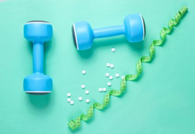 Spor zayıflama konsepti. Dambıllar, cetvel, mavi arka planda haplar. Minimalizm. Üst görünüm