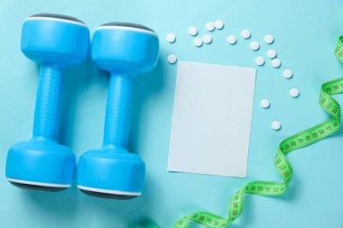 Spor zayıflama konsepti. Dambıllar, cetvel, mavi arka planda haplar. Minimalizm. Fotokopi alanı için beyaz kağıt. Üst görünüm