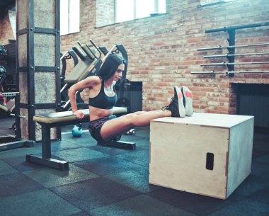 Spor kıyafetli genç esmer trisepsler için yedek kulübesinde şınav çekiyor. Spor salonundaki ağırlığınla antrenman.