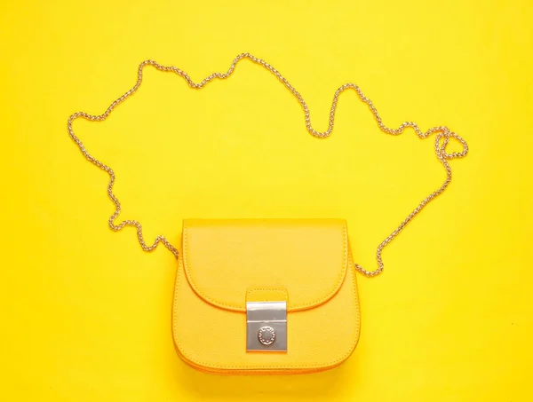 Yellow leather mini bag with chain on yellow background. Minimalism fashion concept. Top view
