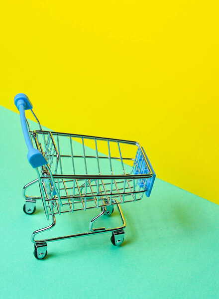 Minimalist shopping concept. Toy shopping trolley on pastel yellow-blue background