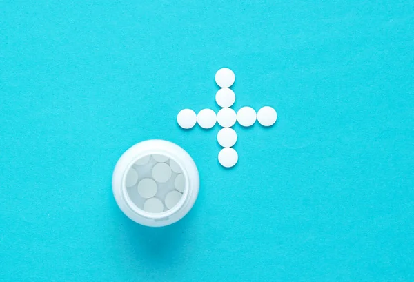 Bottle with pills, white pills in the shape of a cross on a blue background. Top view. Minimalism medical concept. Helping hand