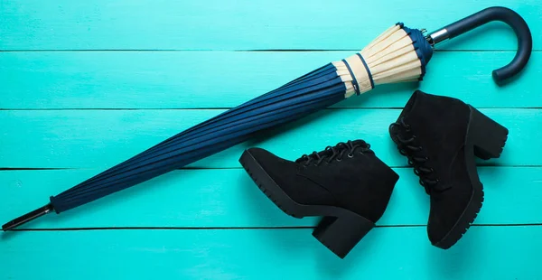 Suede black boots, umbrella on a blue wood background. Top view