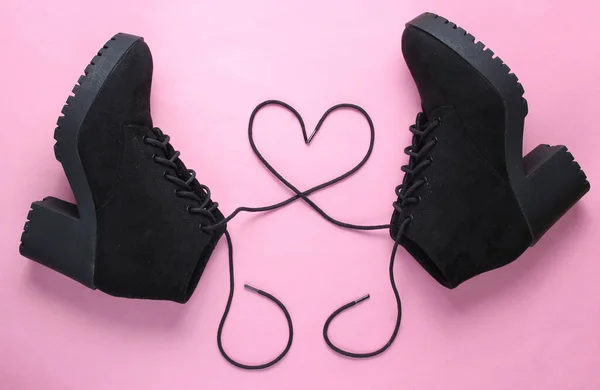 Black suede boots with heart-shaped laces on pink background. Top view