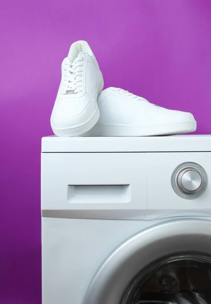 Çamaşır makinesindeki beyaz moda spor ayakkabıları mor arka planın arka planına karşı.