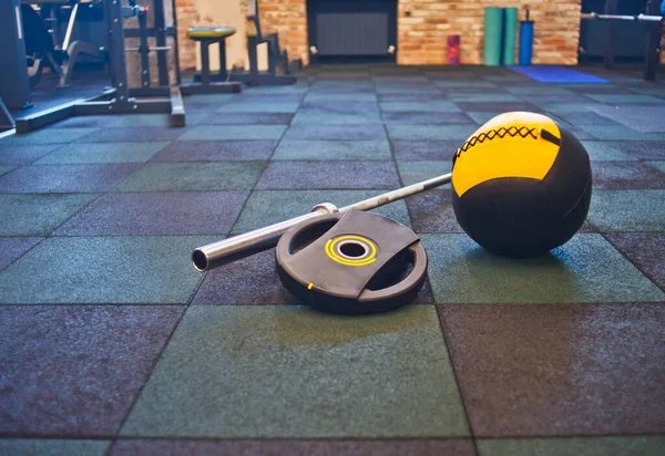 Disassembled barbell, medicine ball lying on floor in the gym. Sports equipment for workout with free weight. Functional training